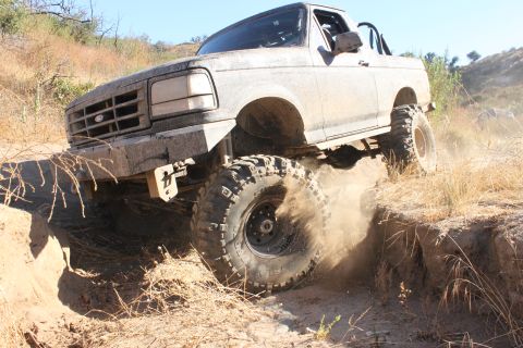 1992 Ford Bronco - This 1992 Ford Bronco navigates a challenging off-road trail, its tires kicking up dust as it climbs the embankment.
