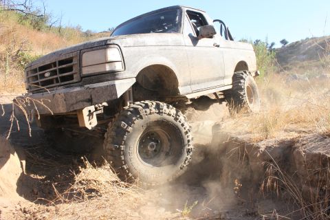 1992 Ford Bronco - Modified 1992 Ford Bronco tackling an off-road obstacle, kicking up dust.