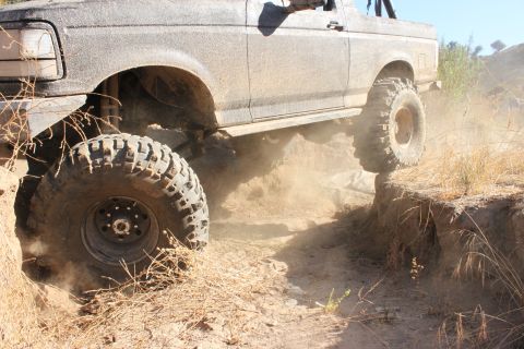 1992 Ford Bronco - A 1992 Ford Bronco navigates a challenging off-road trail, kicking up dust.