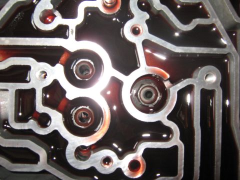 2001 Ford Expedition - Close-up of a transmission valve body filled with red fluid, showing intricate channels and openings.