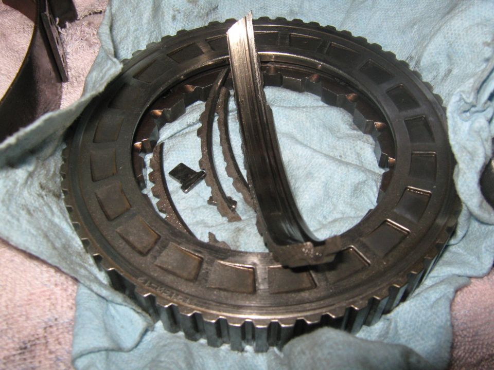 Damaged transmission clutch pack with bent metal plates and broken teeth on a blue cloth
