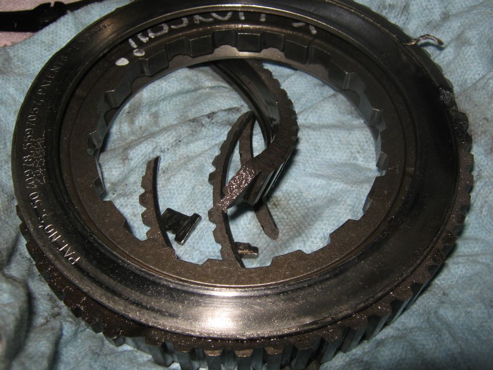 Damaged transmission gear ring with broken teeth, resting on a blue cloth