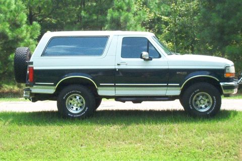 1992 Ford Bronco - This two-tone Ford Bronco is parked on a grassy area with trees in the background.