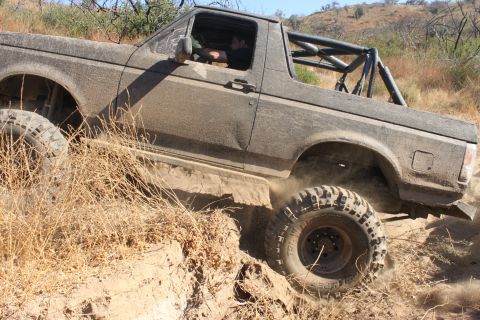 1992 Ford Bronco - A 1992 Ford Bronco navigates a challenging off-road trail, its tires churning through the dirt.