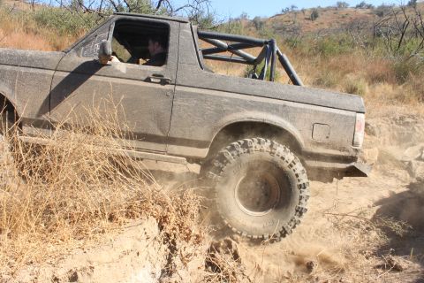 1992 Ford Bronco - A 1992 Ford Bronco navigates a challenging off-road trail, its tires churning through dirt and dust.