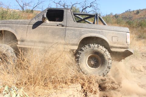 1992 Ford Bronco - A 1992 Ford Bronco navigates a challenging off-road trail, with dry brush and dirt visible.