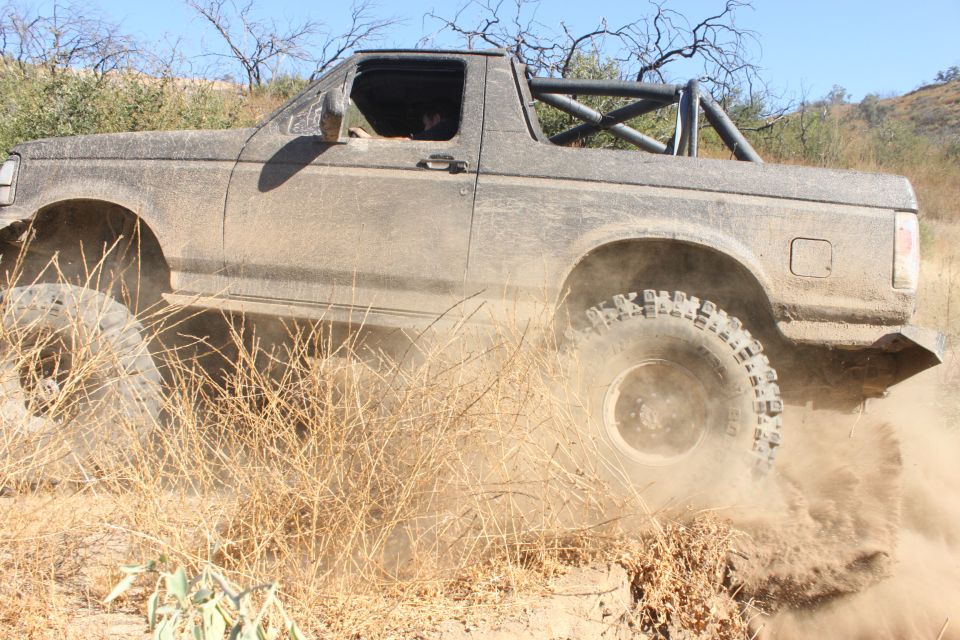 Mud-covered 1992 Ford Bronco driving off-road, kicking up dust
