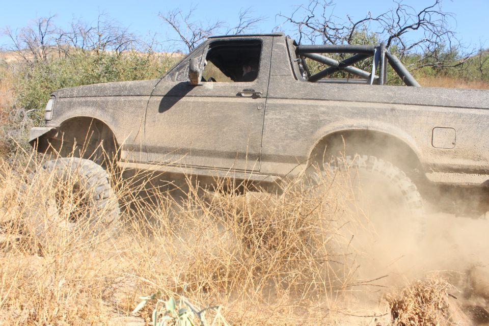 Mud-covered 1992 Ford Bronco with roll cage driving off-road