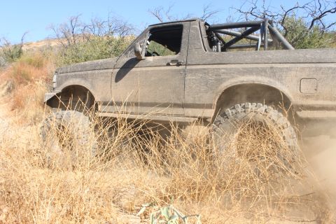 1992 Ford Bronco - Muddy 1992 Ford Bronco navigates rough terrain with a roll cage visible.