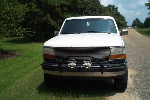 1992 Ford Bronco - Frontal view of a white 1992 Ford Bronco parked on a grassy shoulder next to a paved road.