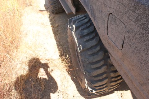 1992 Ford Bronco - A vehicle's large tire is shown on a dirt path, with another vehicle in the background.