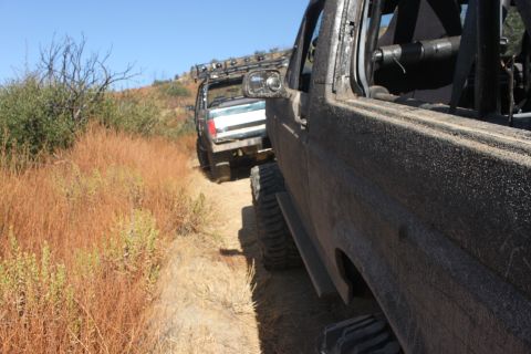 1992 Ford Bronco - Two modified off-road vehicles navigate a dry, grassy trail under a clear blue sky.