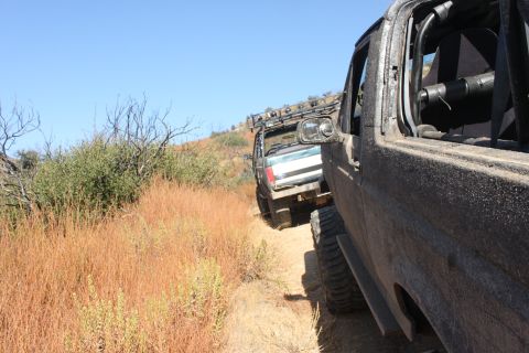 1992 Ford Bronco - Two off-road vehicles navigate a dry, grassy trail under a clear blue sky.