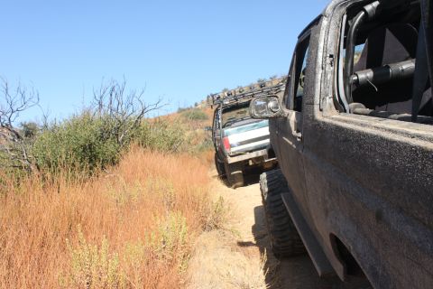1992 Ford Bronco - Two off-road vehicles navigate a dusty trail under a clear blue sky.