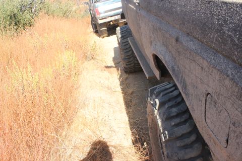 1992 Ford Bronco - Two off-road vehicles, including a 1992 Ford Bronco, navigate a dusty trail through dry vegetation.
