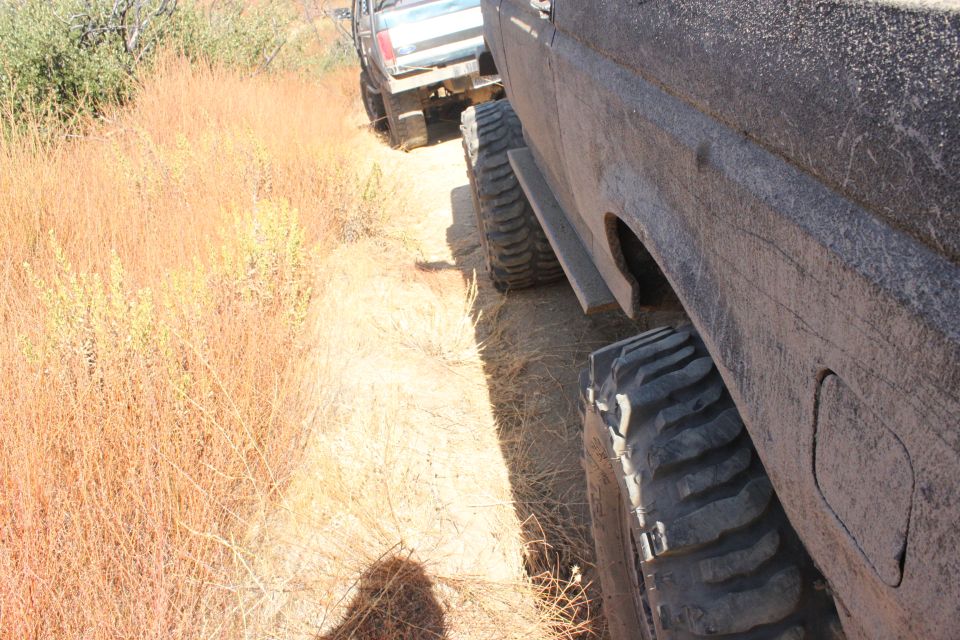 Mud-covered 1992 Ford Bronco side view, with large off-road tires and a second vehicle behind it on a dry, grassy trail