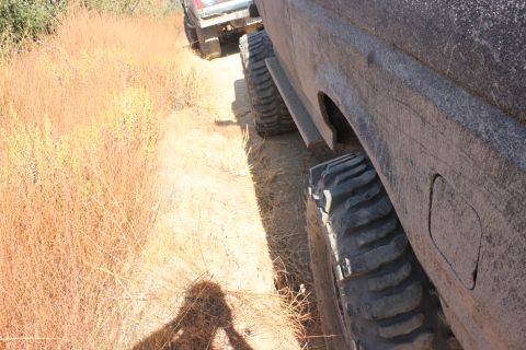 1992 Ford Bronco - Two vehicles navigate a dusty, overgrown trail, highlighting the tires and side profile of the lead SUV.