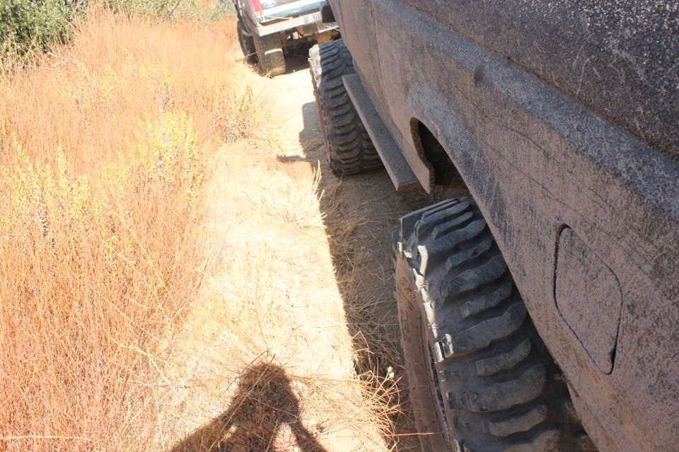 Side view of a muddy SUV with large tires on a dirt trail, another vehicle behind