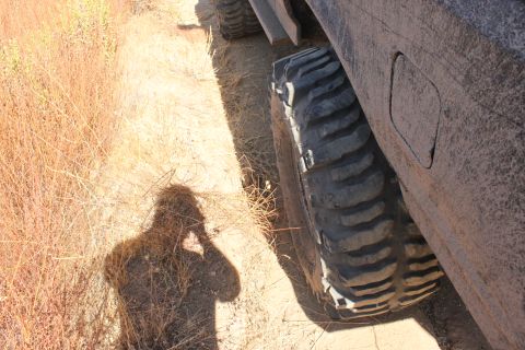 1992 Ford Bronco - A large, aggressive tire on an off-road vehicle sits on a dusty trail next to dry brush.