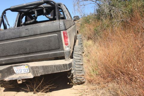 1992 Ford Bronco - This black SUV, likely from the 1980s, navigates a dry, brush-lined trail.