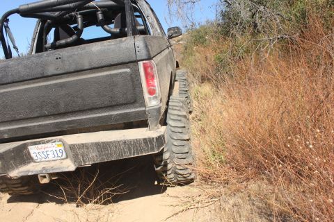 1992 Ford Bronco - This black SUV, equipped with a roll cage and off-road tires, navigates a dusty trail.
