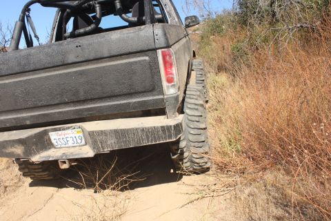 1992 Ford Bronco - Rear view of a 1992 Ford Bronco driving off-road on a dirt path with dry brush.