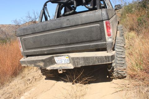 1992 Ford Bronco - This black Ford Bronco, likely from the 1980s, is shown from the rear on a dusty trail.