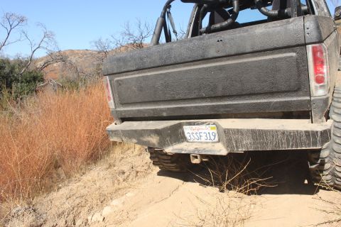 1992 Ford Bronco - Rear view of a 1992 Ford Bronco on a dirt trail with dry brush and hills in the background.