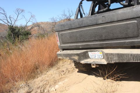 1992 Ford Bronco - The rear of a black Ford Bronco is seen on a dusty trail, with dry vegetation and hills under a clear blue sky.