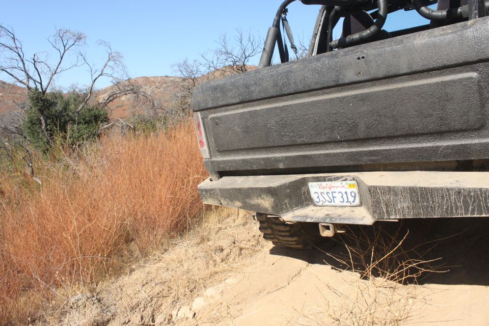 Rear view of a black Ford Bronco on a dirt trail with dry grass and hills in the background. California license plate 3SSF319 is visible