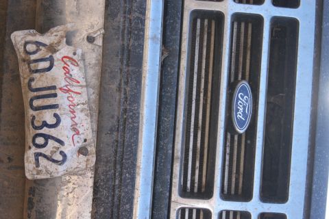 1992 Ford Bronco - A close-up of a Ford emblem on a vehicle's grille, with a dirty license plate nearby.