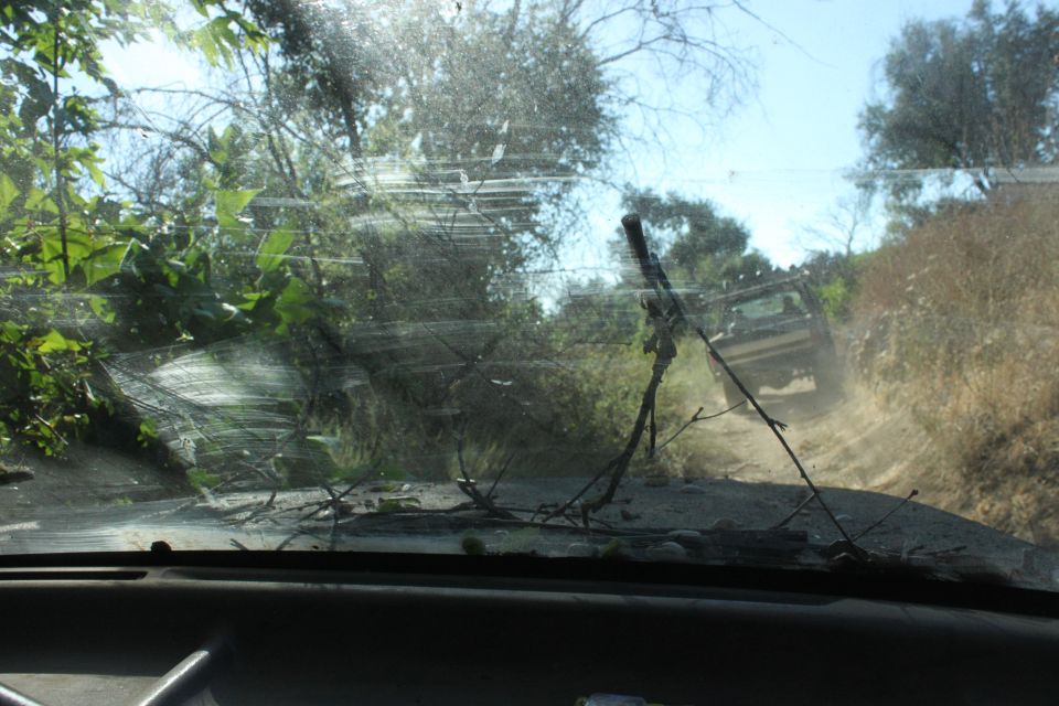 View from inside a vehicle looking out windshield at another vehicle driving up a dusty dirt road