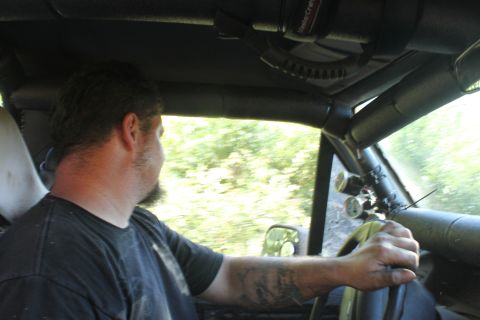 1992 Ford Bronco - Interior view of a man driving a heavily modified vehicle with aftermarket gauges and a roll cage.