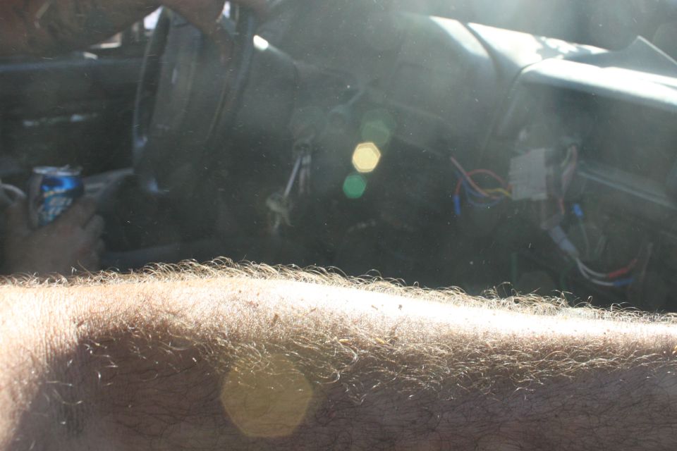 view of car interior, showing steering wheel, dashboard, and exposed wires. A can of soda is visible
