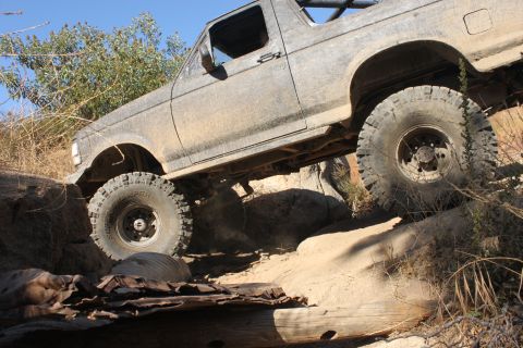 1992 Ford Bronco - This SUV is shown off-roading on a challenging, rocky terrain under a clear blue sky.