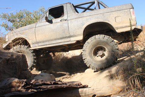 1992 Ford Bronco - A 1992 Ford Bronco navigates a challenging off-road trail with large tires and a roll cage.