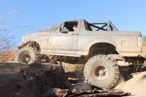1992 Ford Bronco - This 1992 Ford Bronco is shown off-roading on a dirt trail with large tires and a roll cage.