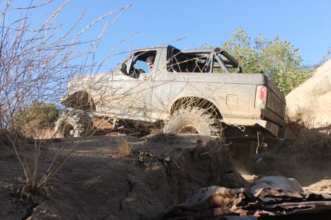 1992 Ford Bronco - A gray 1992 Ford Bronco navigates a rocky, off-road trail with a roll cage installed.