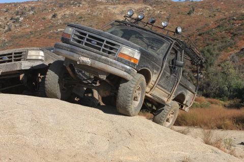 1992 Ford Bronco - A black 1992 Ford Bronco navigates a steep, rocky incline on a dirt trail, with another vehicle partially visible behind it.