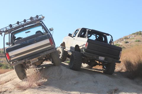 1992 Ford Bronco - Two Ford Broncos tackle a steep, rocky incline under a clear blue sky.