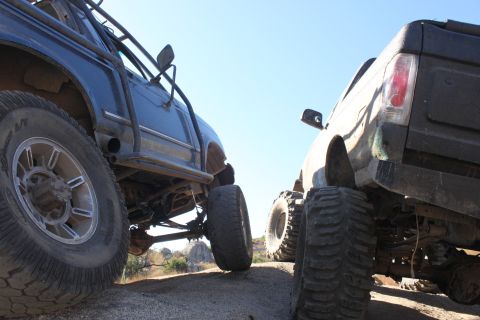 1992 Ford Bronco - Two modified trucks are positioned on a rocky surface under a clear blue sky.
