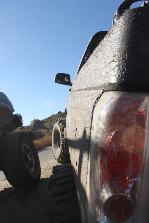 1992 Ford Bronco - Two off-road vehicles are parked on a dirt road with a clear blue sky overhead.