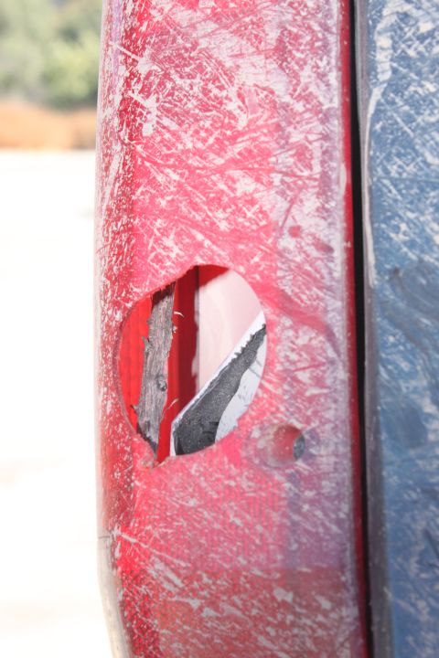 1992 Ford Bronco - Close-up of damaged red and blue vehicle body panels, with a hole revealing internal structure.