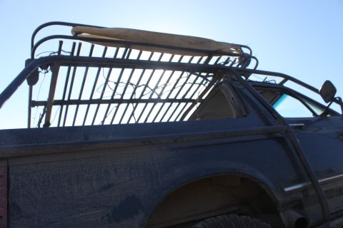 1992 Ford Bronco - Close-up of a custom roll cage and rack on a dark, dusty off-road vehicle under a clear sky.