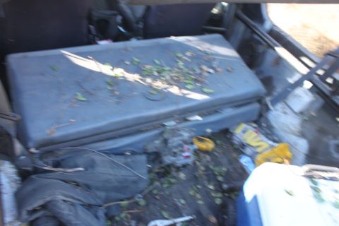 1992 Ford Bronco - The interior of a vehicle shows a folded rear seat with leaves and debris scattered on the floor, along with some yellow containers.