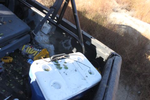 1992 Ford Bronco - Vehicle bed contains a cooler, yellow tool, and other items, with dry vegetation visible.