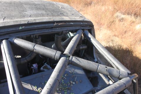 1992 Ford Bronco - The interior of a modified vehicle, a prominent roll cage and exposed engine parts, sits in a dry, grassy outdoor setting.