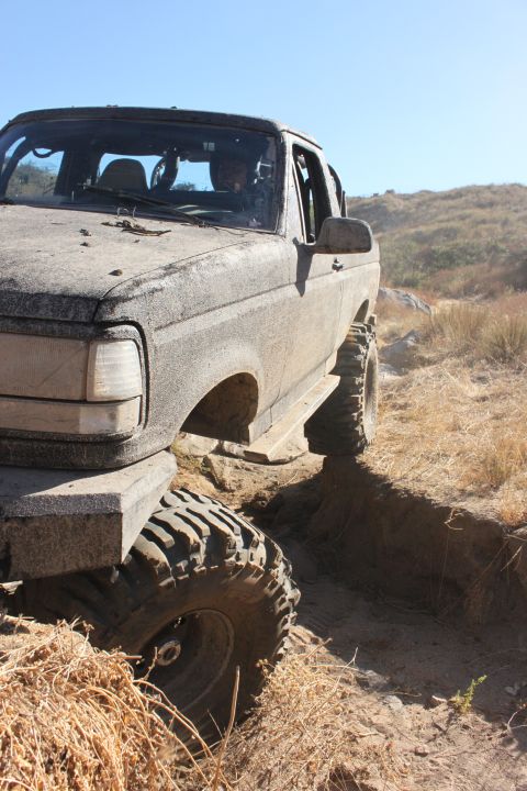 1992 Ford Bronco - Mud-covered 1992 Ford Bronco navigating a challenging off-road trail.