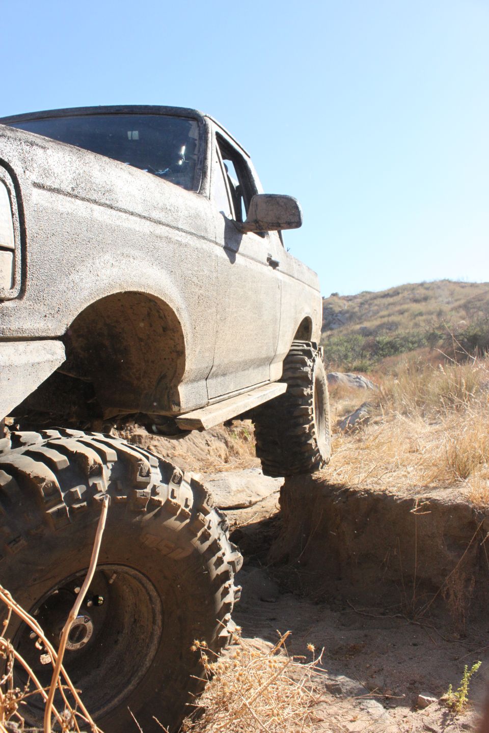 Mud-covered 1992 Ford Bronco with large off-road tires climbing a dirt embankment