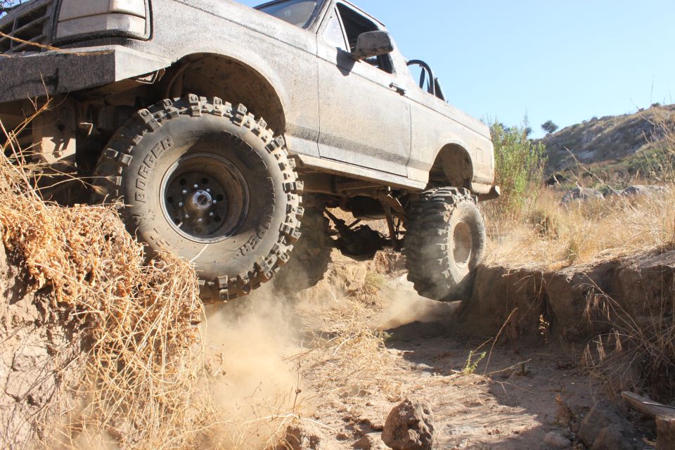 Modified 1992 Ford Bronco climbing a steep dirt embankment, kicking up dust